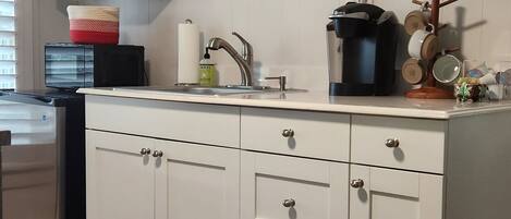 A kitchen with white cabinets, a stainless steel sink, a coffee maker, and a decorative mirror.