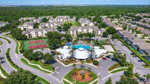 An aerial view of a residential community with apartment buildings, a central pool, tennis courts, and a landscaped central area.