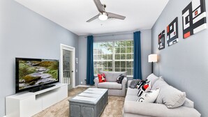 A modern living room with a flat-screen TV, grey sofa, and a ceiling fan.