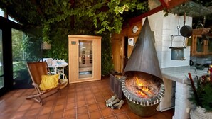 Eine Terrasse im Freien mit einem Fliesenboden aus Stein, einer hängenden Feuerstelle, einem Holzstuhl mit gelber Sitzkissen und einer Holzkabine mit Glastüren.