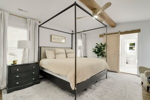 A bedroom with a four-poster bed, a dark dresser, a bedside lamp, and a ceiling fan.