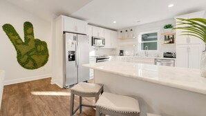 Una cocina moderna con armarios blancos, encimera de mármol y una original pieza de arte mural verde.