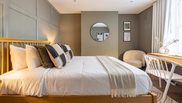 Een moderne hotelkamer met een groot bed, een ronde spiegel, een bureau met stoel en een raam met gordijnen.