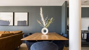 A modern dining area with a wooden table, blue chairs, and a vase with dried plants. - The Nine Elms Lane Arms - Stunning & Bright 2bdr Flat With Balconies (London)
