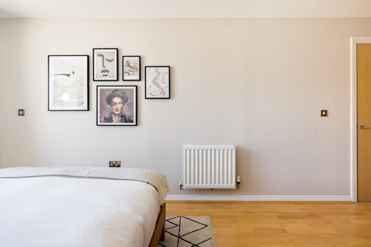 A bedroom with a bed, a radiator, and four framed artworks on the wall.