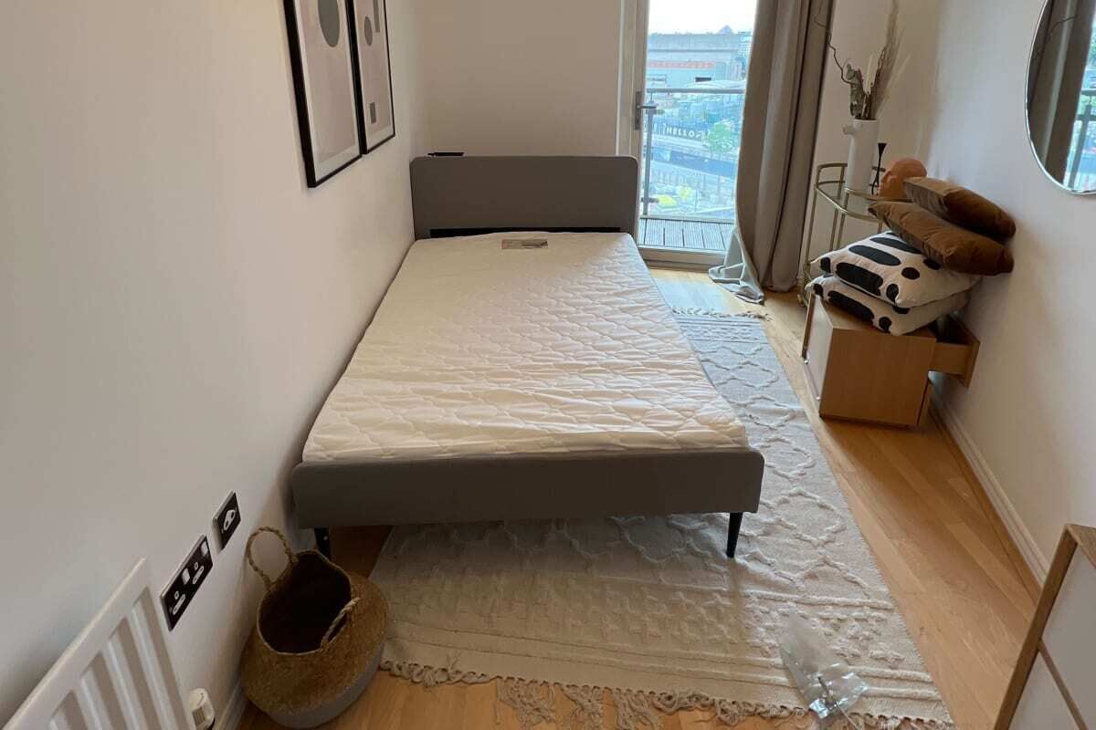 Ein kleines, ordentliches Schlafzimmer mit einem Einzelbett, einem Nachttisch, einem Fenster mit Blick und einer Heizung.