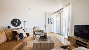 A modern living room with a leather sofa, a coffee table, a TV, and a large window with curtains. - The Nine Elms Lane Arms - Stunning & Bright 2bdr Flat With Balconies (London)
