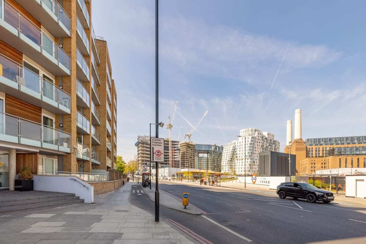 A modern urban street with multi-story residential buildings, a clear sky, and a parked car.