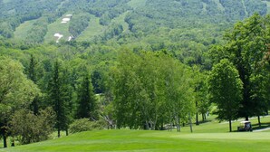 Een golfbaan met een heuvelachtig achtergrondlandschap, bomen en een heldere lucht.