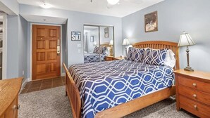 Een slaapkamer met een bed, nachtkastje, houten dressoir, plafondventilator en een deur.