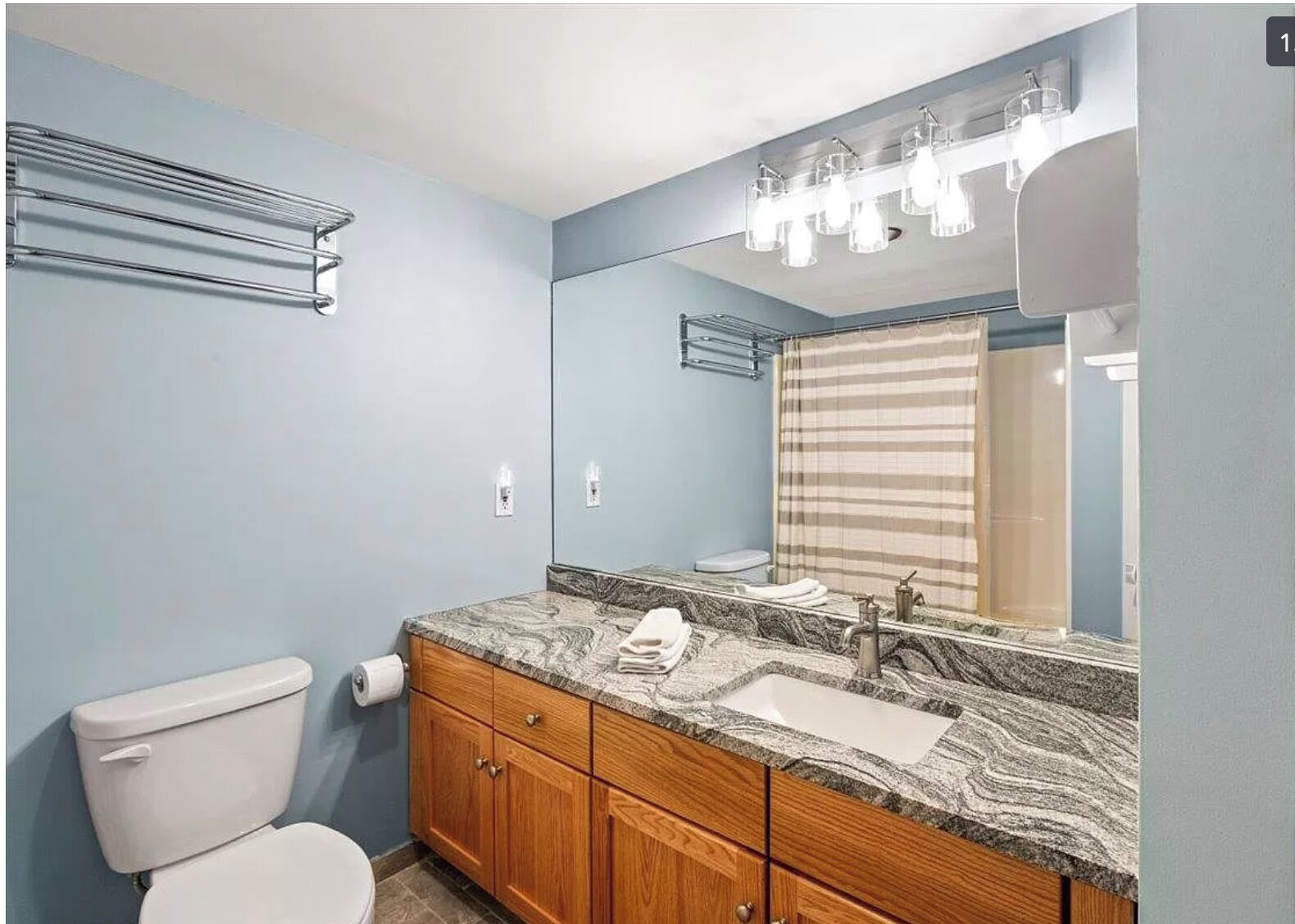 Une salle de bain avec un comptoir en marbre, des meubles en bois, des toilettes blanches et un rideau de douche à rayures.