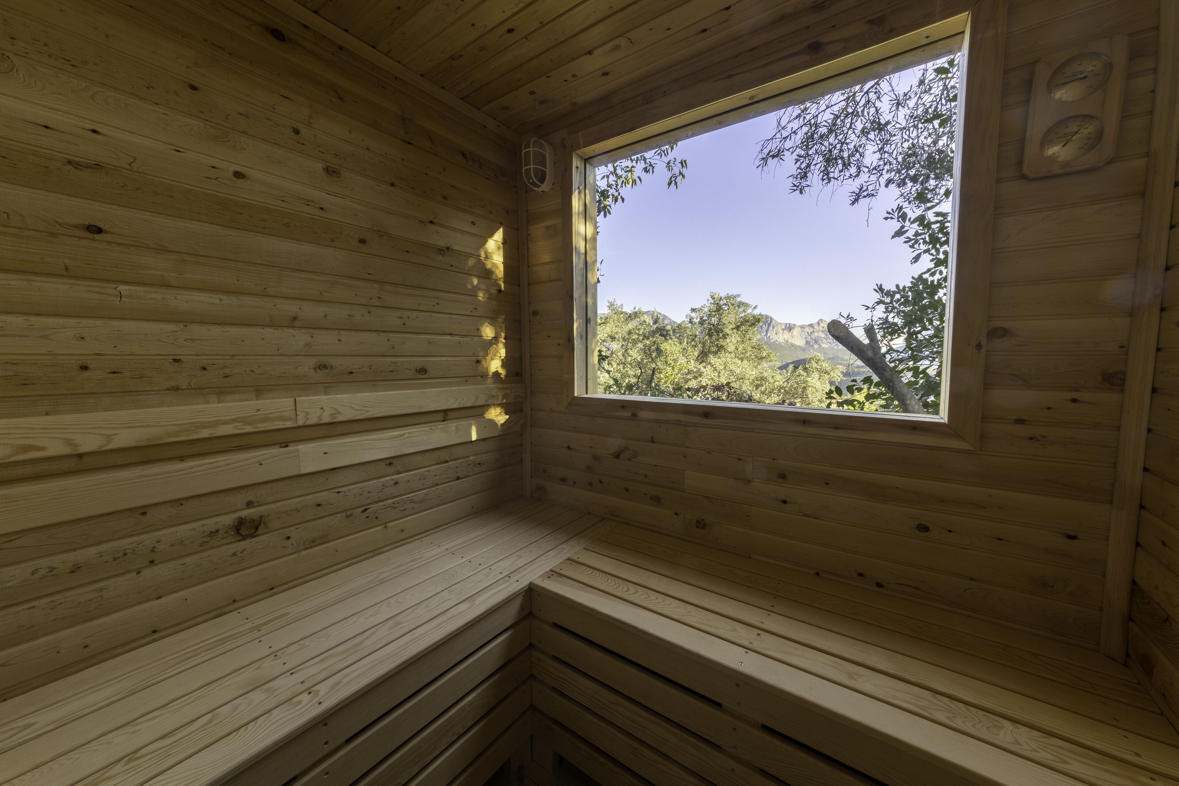A wooden cabin room with a bench, a window, and a wall clock.