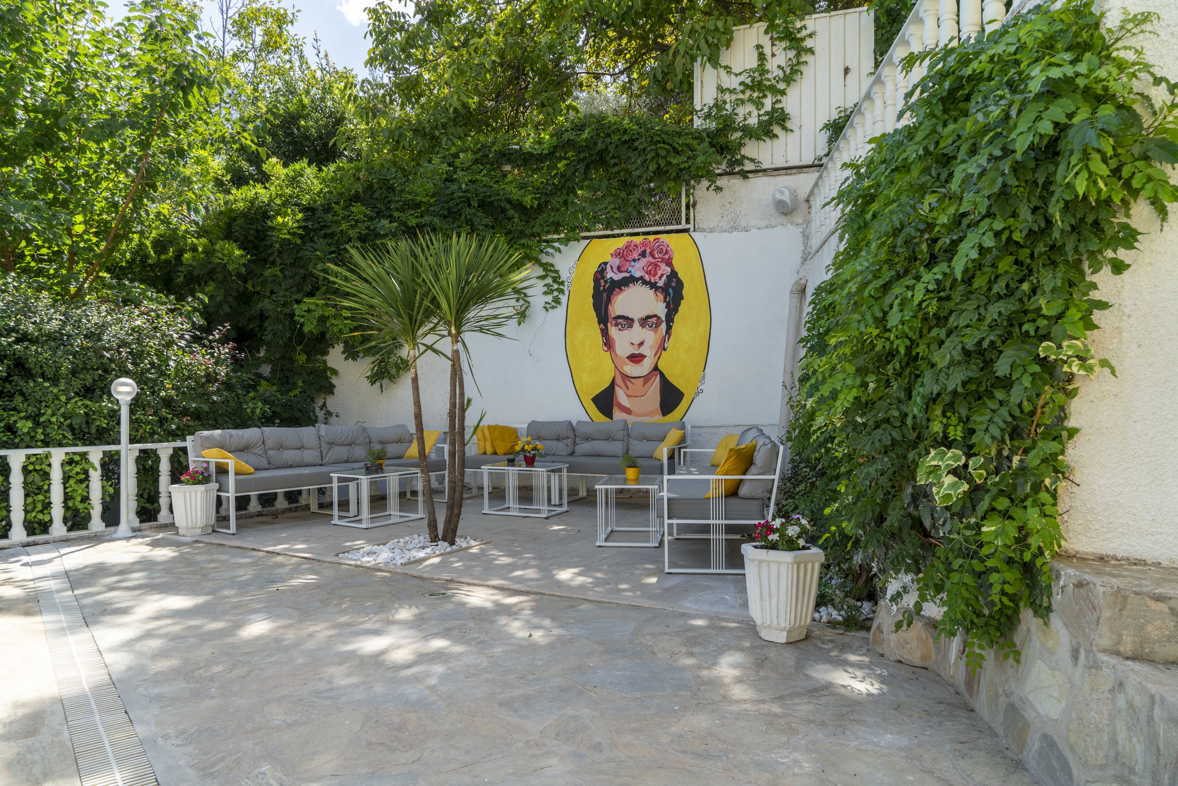An outdoor seating area with a mural, stone flooring, and greenery.