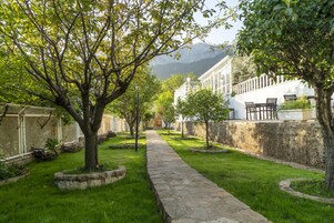 A stone pathway leading to a building with a white facade and a mountain in the background.