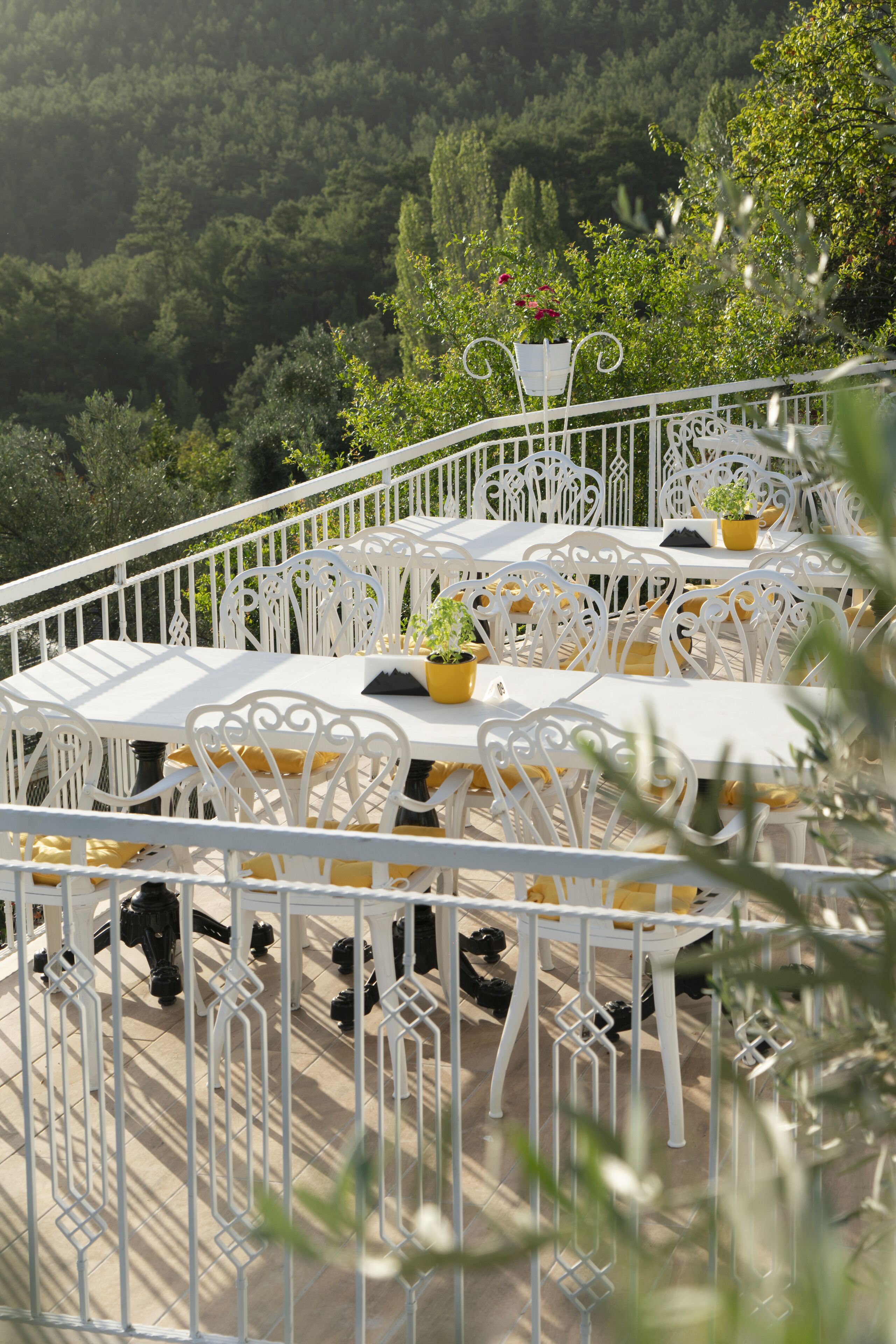An outdoor dining area with white metal tables and chairs, surrounded by a white metal railing.
