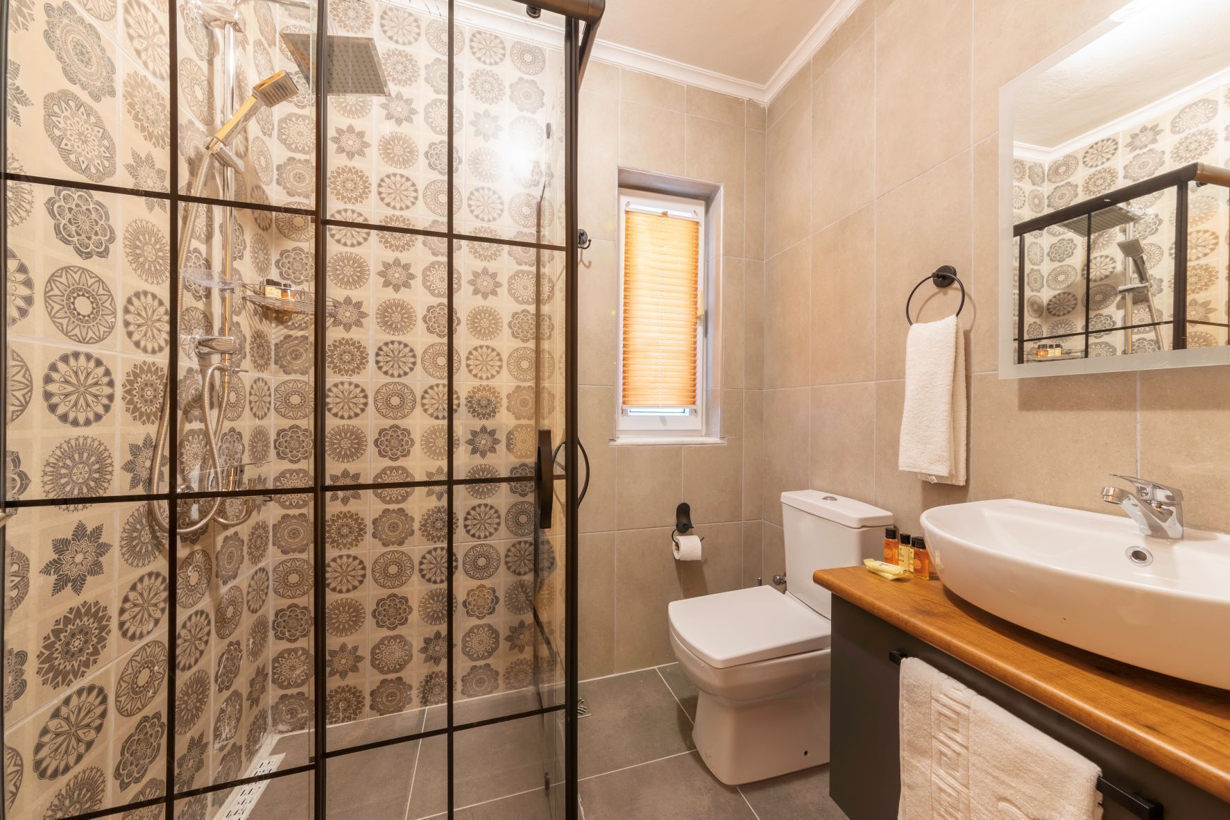 Un baño con azulejos estampados, cabina de ducha, inodoro y lavamanos con espejo.