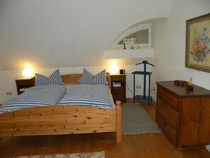 A bedroom with a wooden bed, two bedside tables with lamps, a dresser, and a mirror above the bed. - Rügenferien Unter Reet auf Großem Wassergrundstück (Garz/Rügen)