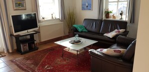 Ein Wohnzimmer mit Fernseher auf einem Schrank, einem Ledersofa, einem Couchtisch und einem roten Teppich mit Muster.