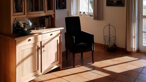 Une pièce avec un meuble en bois, une chaise noire, une fenêtre avec des rideaux et un sol carrelé.