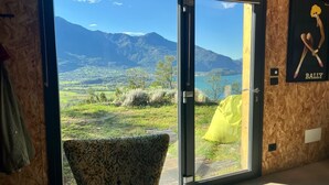 A room with a large sliding glass door leading to a scenic view of mountains and a lake. - COTTAGE ORSOLA by KlabHouse-4pax w/AC and Lakeview (Dolo)