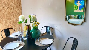 A dining area with a round table set for four, a green vase with flowers, a bottle of wine, and a mirror with a green wall in the background. - COTTAGE ORSOLA by KlabHouse-4pax w/AC and Lakeview (Dolo)