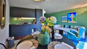 A dining area with a table set for two, a vase of flowers, and a modern kitchen in the background. - COTTAGE ORSOLA by KlabHouse-4pax w/AC and Lakeview (Dolo)