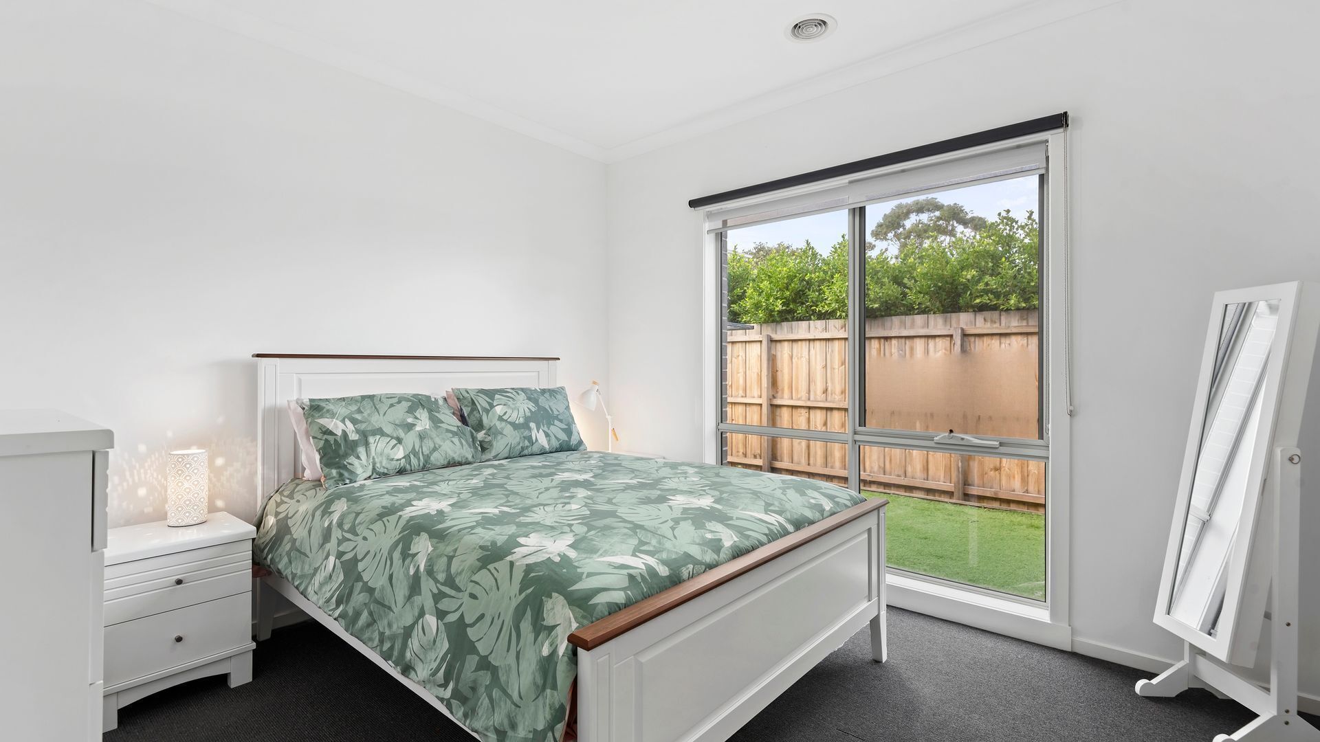 A bedroom with a bed, a nightstand, a lamp, and a large sliding glass door leading to a backyard.