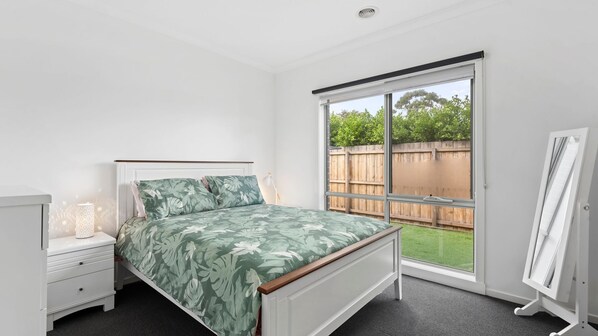 A bedroom with a bed, a nightstand, a lamp, and a large sliding glass door leading to a backyard.