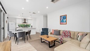 Una sala moderna con un sofá, una mesa de centro y una zona de comedor con sillas, y una cocina al fondo.
