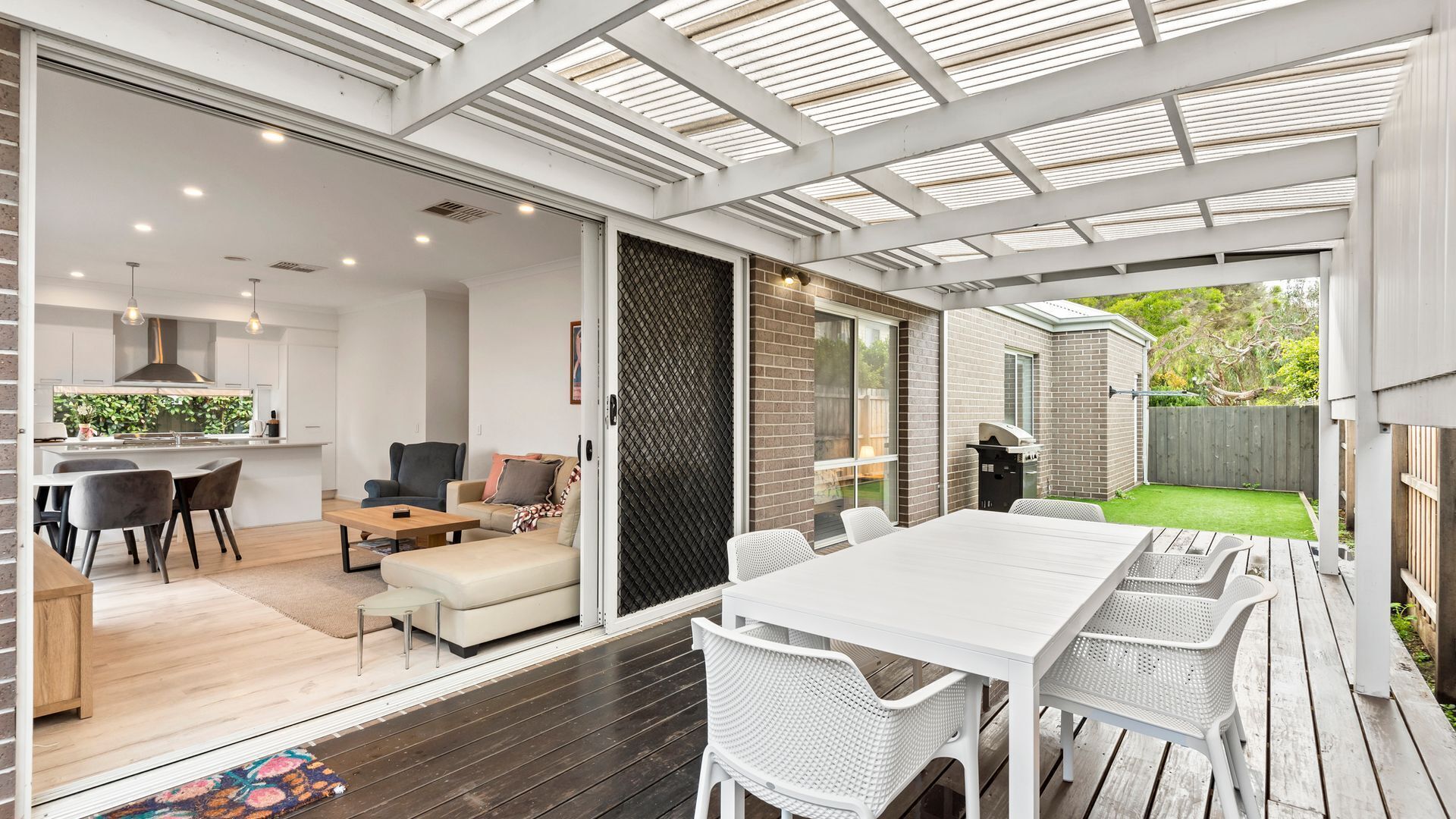 Een moderne keuken met witte kastjes, een eethoek met een witte tafel en stoelen, en een overdekt terras met een barbecue.
