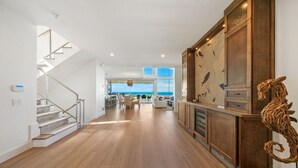 A spacious interior with a wooden staircase, a dining area with a view, and a kitchen with wooden cabinets and a decorative piece. - Luxury Beachfront on the Sand of Gulf of Mexico (Anna Maria)