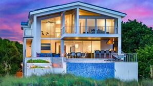 A modern two-story house with large glass windows, a balcony, and outdoor seating. - Luxury Beachfront on the Sand of Gulf of Mexico (Anna Maria)