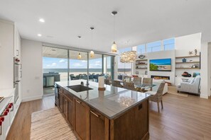 Een moderne keuken met een groot schiereiland, een eethoek met stoelen en uitzicht naar buiten.