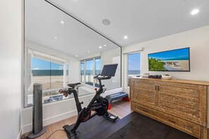 A modern home gym with a stationary bike, a treadmill, and a large window overlooking the beach. - Luxury Beachfront on the Sand of Gulf of Mexico (Anna Maria)