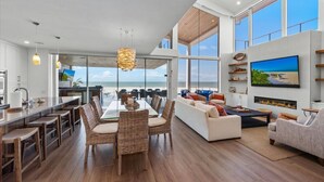 A spacious living area with a large dining table, wicker chairs, a white sofa, and a TV mounted on the wall. - Luxury Beachfront on the Sand of Gulf of Mexico (Anna Maria)