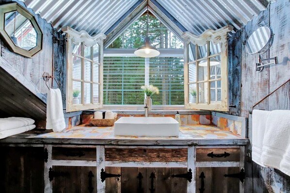 A rustic bathroom with a large window, a sink, and a mirror. - Lazy Dog Retreat at GratiDude Ranch Nevada City (Nevada City)