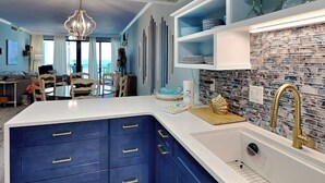 A modern kitchen with blue cabinets, a white countertop, and a tiled backsplash. - A Joyful Breeze | Beachfront, Pool, Grills, Fun! (Navarre Beach)