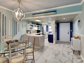 Uma cozinha moderna com armários brancos, piso de mármore e área de jantar com mesa de vidro e cadeiras de madeira.