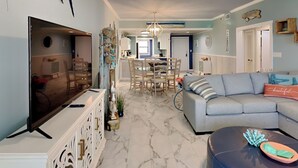 A spacious living room with a large flat-screen TV, a blue sofa, and a marble-patterned floor. - A Joyful Breeze | Beachfront, Pool, Grills, Fun! (Navarre Beach)