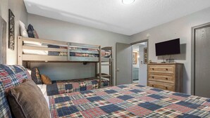 Quarto com cama beliche, televisão de tela plana, cômoda e colcha acolchoada.