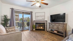 A living room with a fireplace, a television, and a ceiling fan. - Bunker Ridge Rendezvous - Branson - Condo in Pointe Royale (Branson)