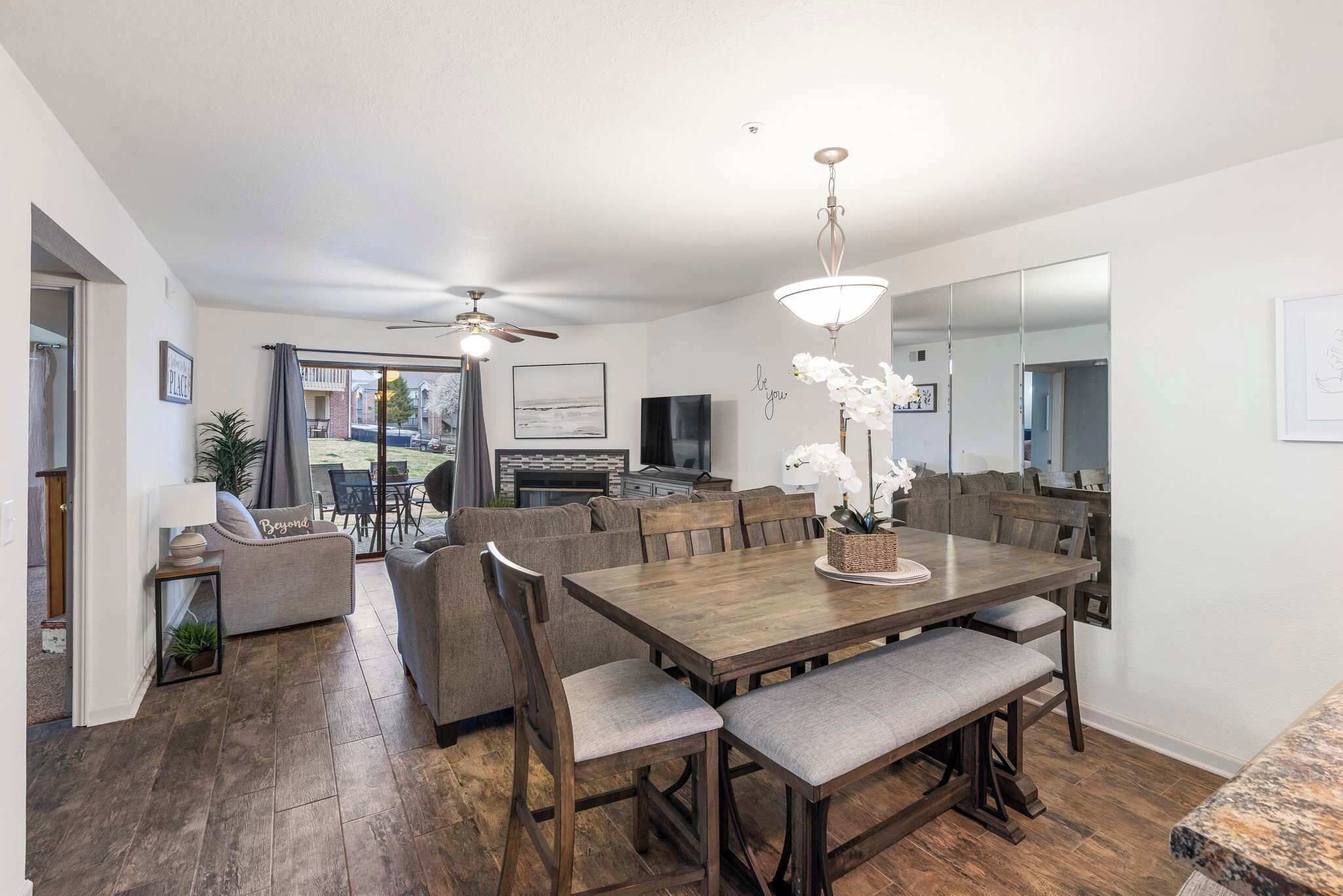 A spacious living room with a wooden dining table, grey sofas, and a large mirror.