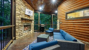Una cabaña de troncos con chimenea de piedra, zona de estar al aire libre y vistas al bosque.