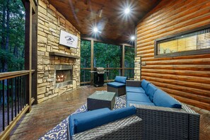 Una cabaña de troncos con chimenea de piedra, zona de estar al aire libre y vistas al bosque.