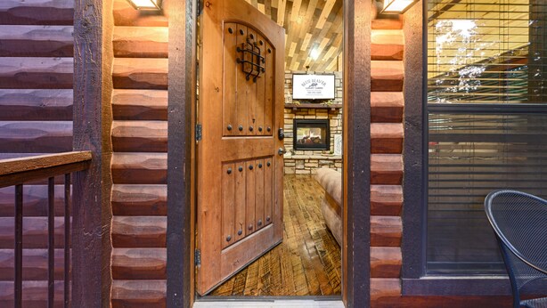 Entrada de una cabaña de madera con puerta de madera, chimenea de piedra y una silla negra junto a la ventana.