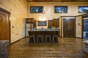 Cocina de cabaña de madera con una isla central, taburetes de bar y encimera de piedra.