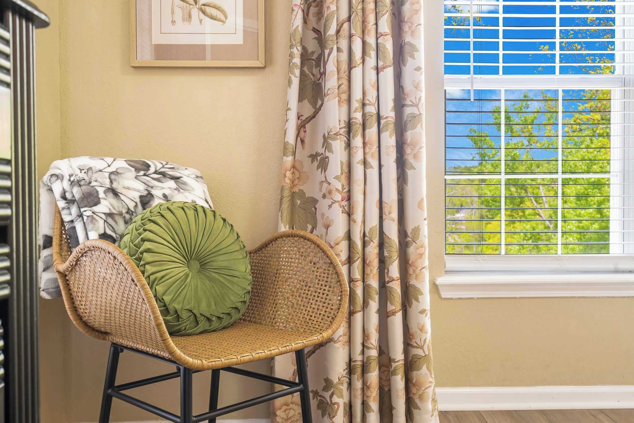 A corner with a wicker chair, a green cushion, and a floral curtain.