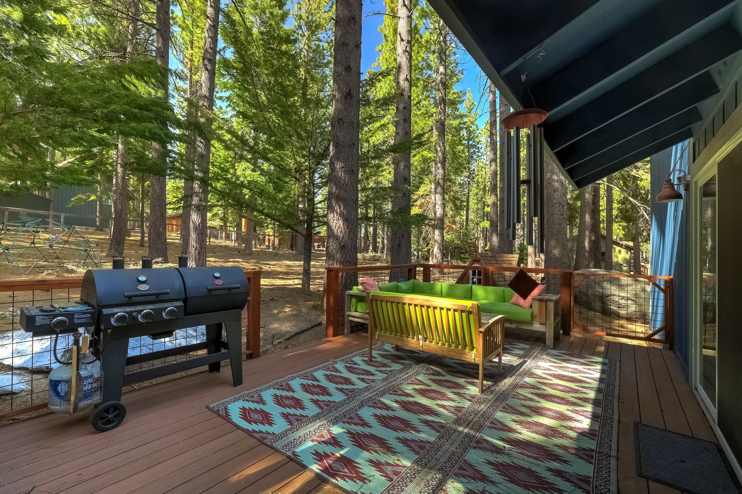 A deck with a grill, a green cushioned bench, and a patterned rug.