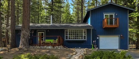 Eine blaue Holzhütte mit einer Terrasse, einem Steinweg und einer Garage.