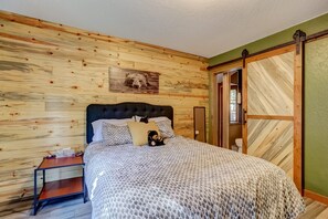A bedroom with a wooden wall, a bed with patterned bedding, a nightstand, and a sliding door.